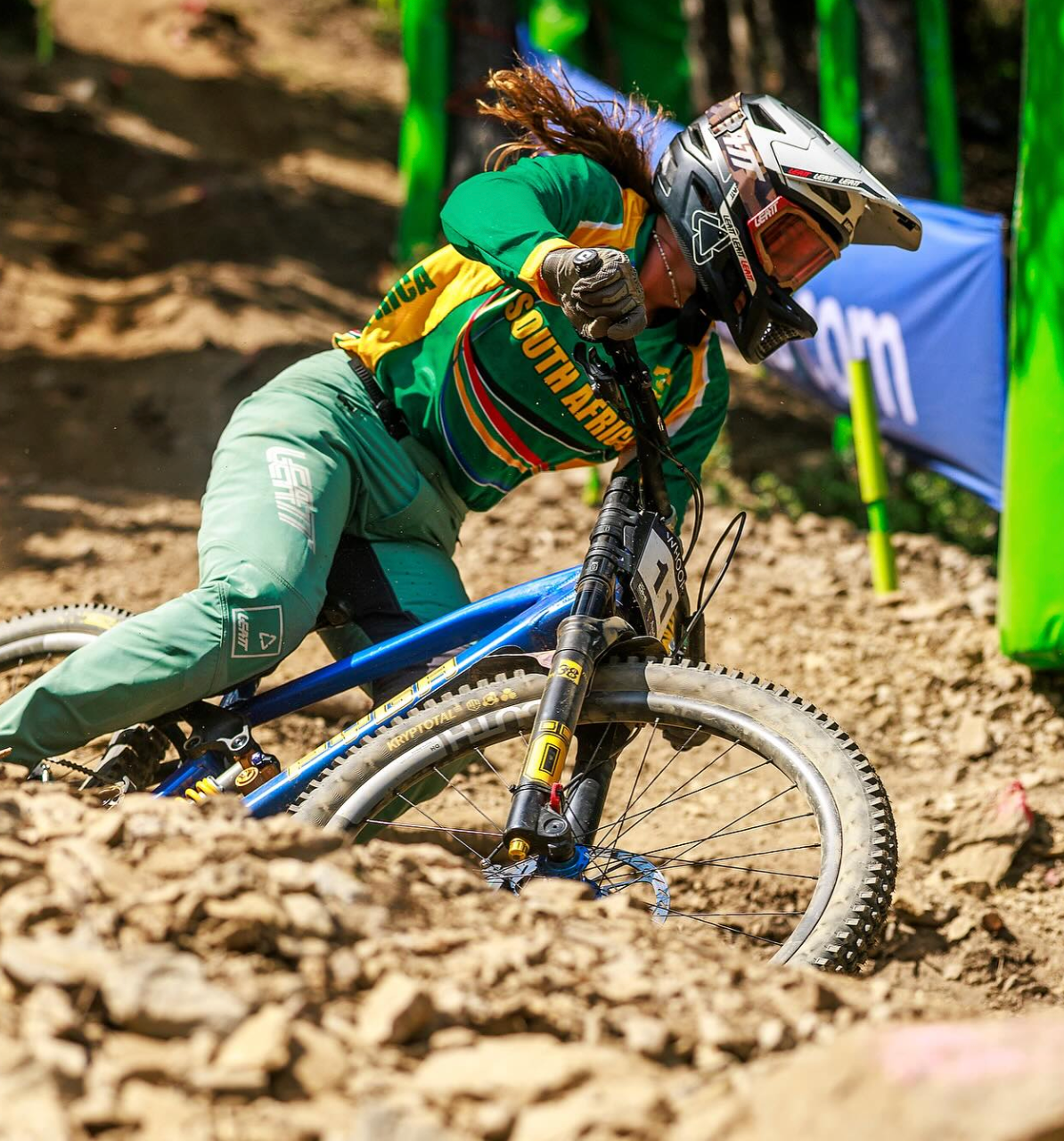 Biker in green and yellow outfit riding a blue bike on a muddy track
